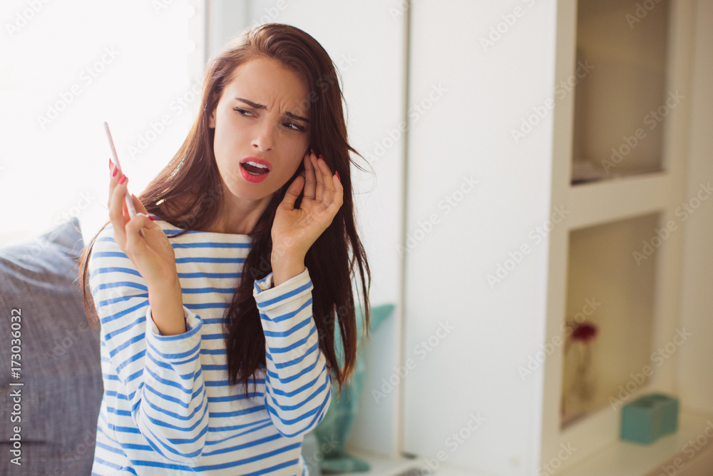 The young disappointed woman sitting on the sofa in the room and keeping phone in hand The young disappointed woman sitting on the sofa in the room and keeping phone in hand