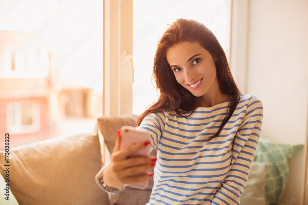 Portrait of young cheerful divine woman who sitting on the sofa in the room and doing selfie-photo with phone Portrait of young cheerful divine woman who sitting on the sofa in the room and doing selfie-photo with phone
