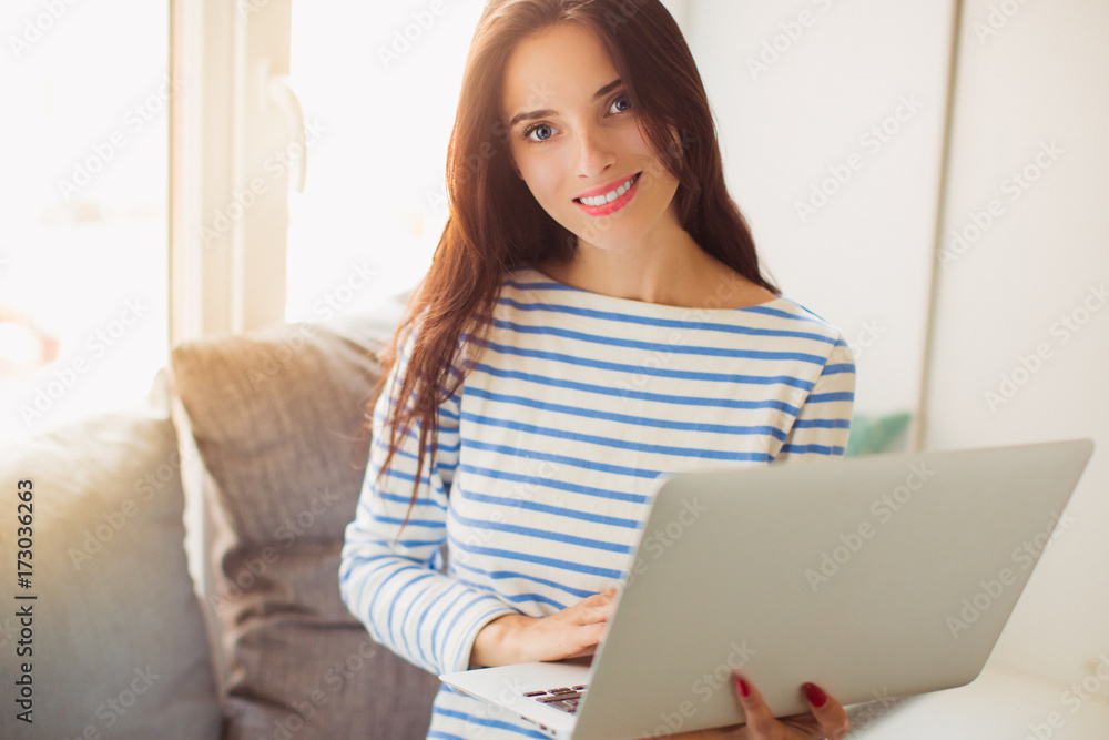 Portrait of young cheerful divine woman who sitting on the sofa in the room and keeping laptop Portrait of young cheerful divine woman who sitting on the sofa in the room and keeping laptop
