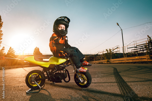 Fototapeta Naklejka Na Ścianę i Meble -  Child on a motorcycle doing moto stunt. Small boy get a difficult and dangerous trick on his small motorcycle. Small biker dressed in a protective suit and helmet.