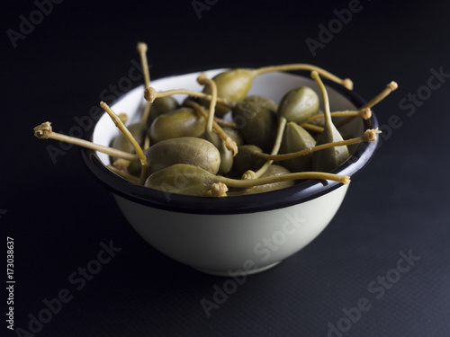 Schilderij op canvas Italian caper berries with stems in small bowl isolated on black background