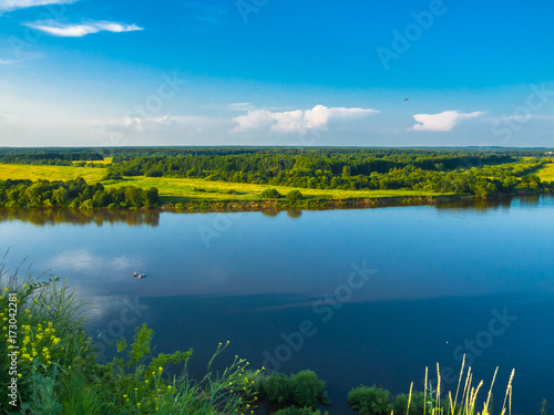 The River Vyatka. Kirov region, Kirov, Russia. Summer water landscape. River, sky, clouds, sun, a fisherman is fishing on a boat.