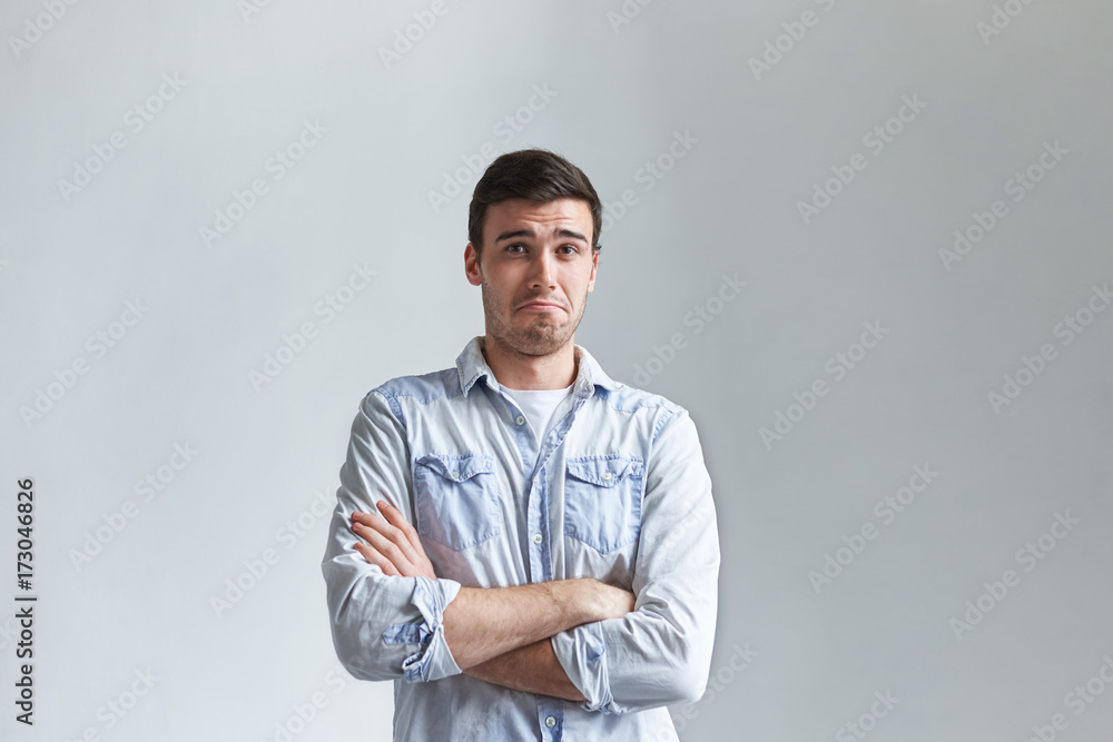 Handsome young male with stubble keeping arms folded, staring at camera with skeptical doubtful facial expression, his look, gesture and grimace expressing disbelief and doubt. Body language Handsome young male with stubble keeping arms folded, staring at camera with skeptical doubtful facial expression, his look, gesture and grimace expressing disbelief and doubt. Body language