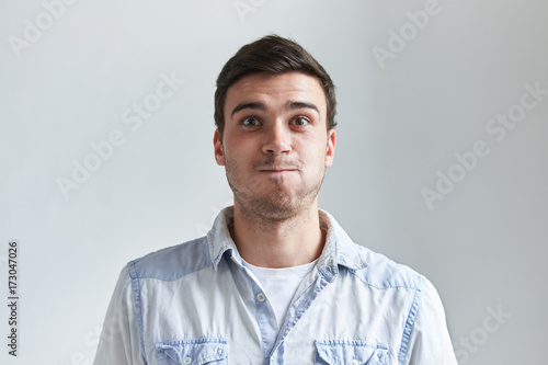 Funny young man grimacing, staring at camera with eyes popped out, inflating cheeks, holding his breath, trying hard not to laugh. Childish bug-eyed guy blowing cheeks, about to burst out laughing