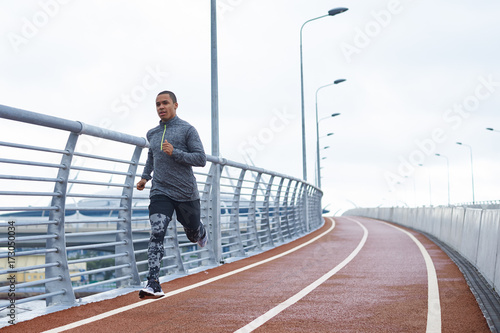 Healthy active lifestyle concept. Attractive young African male jogger exercising at stadium alone early in the morning. Muscular dark-skinned sportsman in trendy outfit, getting ready for marathon