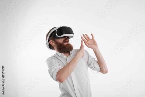 Innovations, augmented reality, futuristic technology and cyberspace. Scared young bearded man in white shirt experiencing 3d reality using oculus rift headset, making stop gesture and screaming