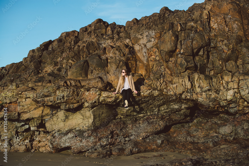 Young woman sitting on seaside rock ledge Young woman sitting on seaside rock ledge