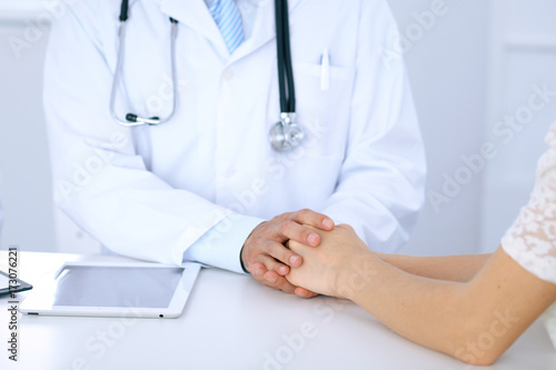 Doctor reassuring his female patient by touching her hands while talking. Symbol of support and trust in medicine