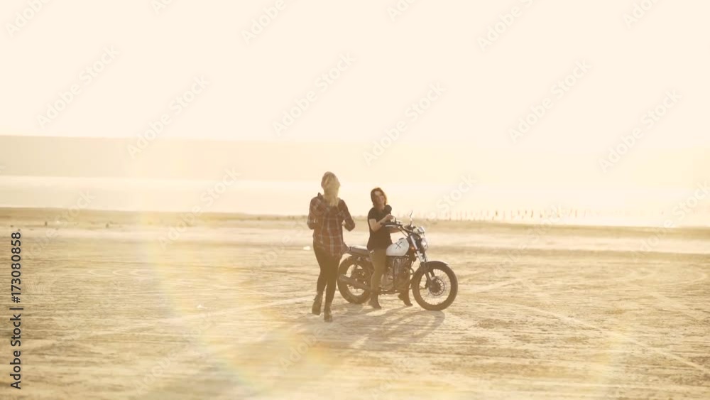 Attractive young woman motorcyclist with his girlfriend riding a motorcycle in a desert on sunset or sunrise. Girlfriends on a bike. Female rider Attractive young woman motorcyclist with his girlfriend riding a motorcycle in a desert on sunset or sunrise. Girlfriends on a bike. Female rider