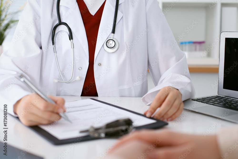 Close up of a female doctor filling up an application form while consulting patient Close up of a female doctor filling up an application form while consulting patient