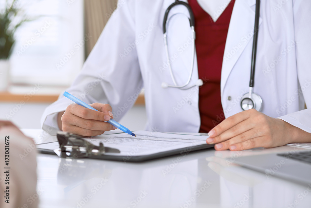 Close up of a female doctor filling up an application form while consulting patient Close up of a female doctor filling up an application form while consulting patient
