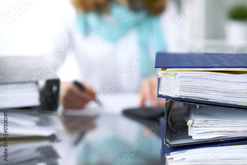 Binders with papers are waiting to be processed with businesswoman or secretary back in blur. Internal Revenue Service inspector checking financial document