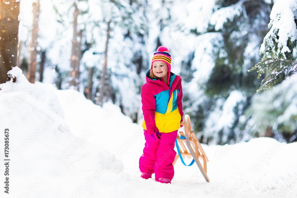 Child playing in snow on sleigh in winter park