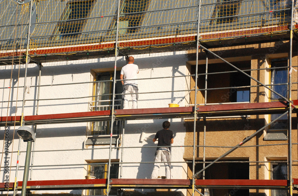 Zwei Maler auf Gerüst streichen Hausfassade weiß an
