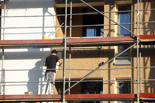 Maler auf Gerüst streicht Hausfassade weiß