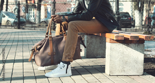 Fashion elegant african man with bag sits on the bench in the park close up