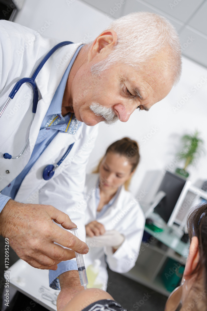 doctor injecting patient nurse in the background doctor injecting patient nurse in the background