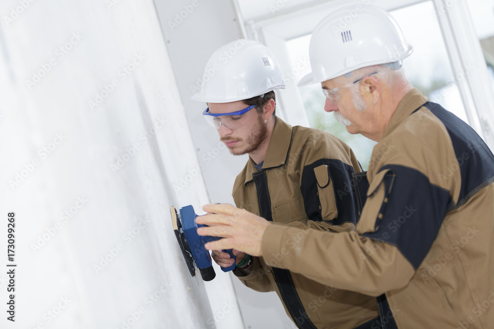 young worker making repair in room with older coleague showing young worker making repair in room with older coleague showing