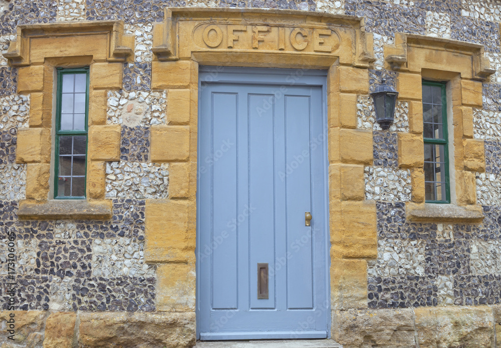Fototapeta premium Light blue wooden doors to an old stone building with an office sign above.