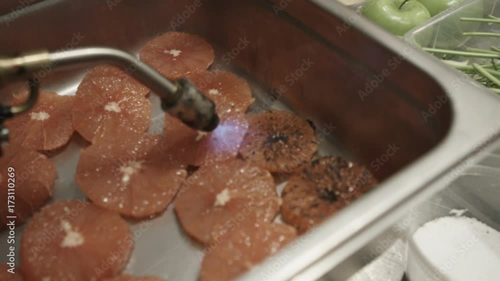 Person sears grapefruit with torch, slow motion