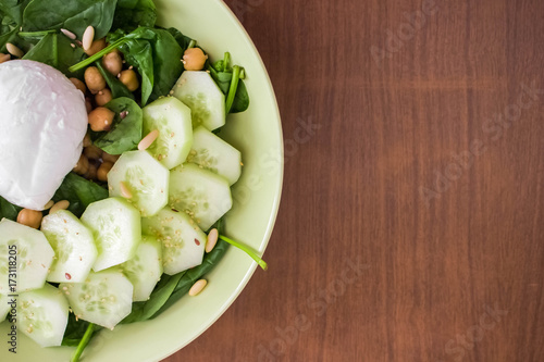 Top view of cucumbers, mozzarella and salad on a plate, with wooden background