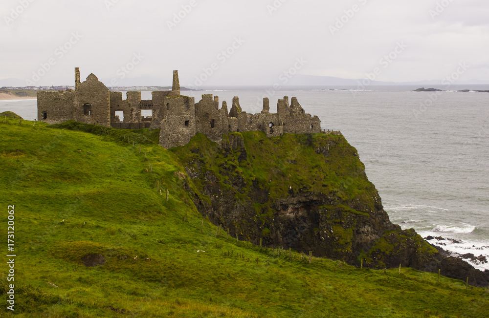 The shadowy  ruins of the medieval Irish Dunluce Castle on the cliff top overlooking the Atlantic Ocean on the north coast of Ireland. Taken on a dull wet day