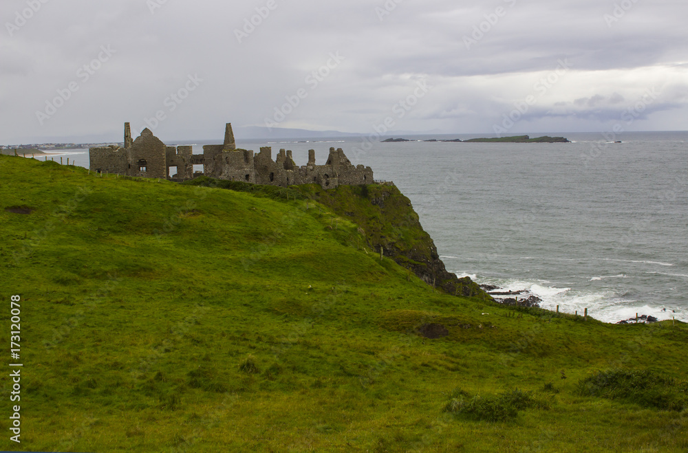 The shadowy  ruins of the medieval Irish Dunluce Castle on the cliff top overlooking the Atlantic Ocean on the north coast of Ireland. Taken on a dull wet day