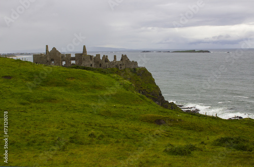 The shadowy ruins of the medieval Irish Dunluce Castle on the cliff top overlooking the Atlantic Ocean on the north coast of Ireland. Taken on a dull wet day