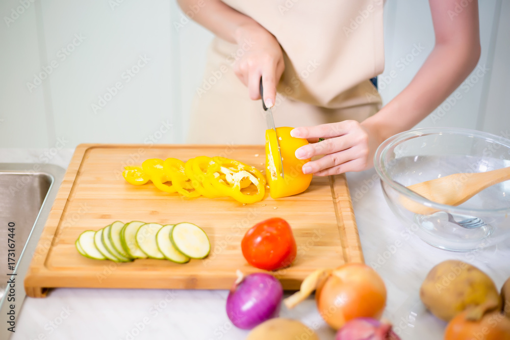 Close up of Asian girl garnishing salads in the kitchen with others garnishing their salads and oil pouring into bowl of salad Close up of Asian girl garnishing salads in the kitchen with others garnishing their salads and oil pouring into bowl of salad