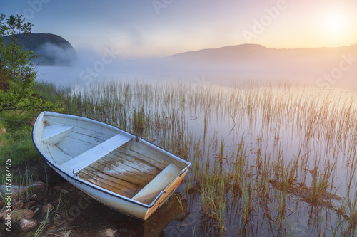 Obraz na plátně Boat on the shore of a misty lake on a summer morning