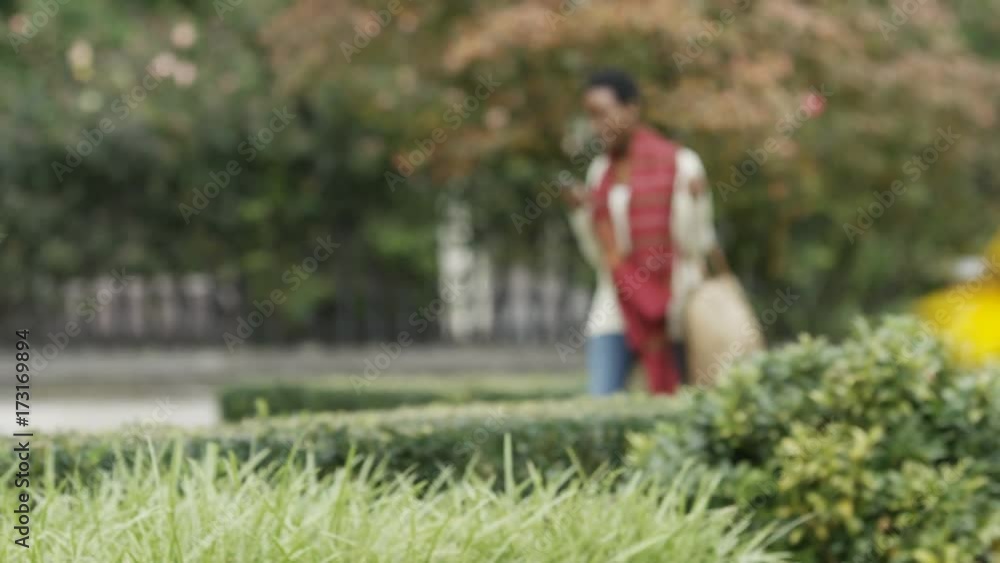 Attractive young black female walks through city gardens whilst reading and typing on her phone Attractive young black female walks through city gardens whilst reading and typing on her phone