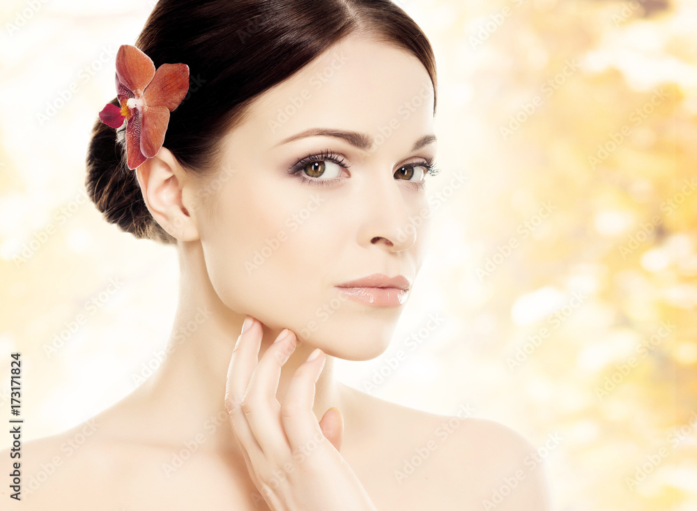Close-up portrait of a beautiful girl with an orchid flower in her hair. Health, treatment, spa concept.