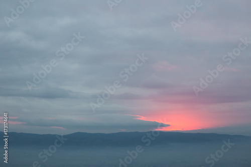 Red sunset filtering through an hole in the overcast sky  with mist filling a valley below