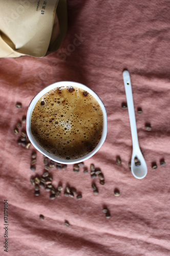 Coffee cup in white pottery mug, scattered coffee beans from paper package