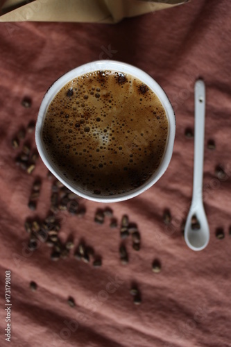 Coffee cup in white pottery mug, scattered coffee beans from paper package