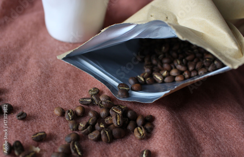 Coffee cup in white pottery mug, scattered coffee beans from paper package
