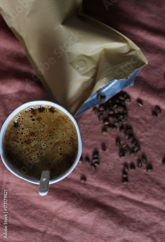 Coffee cup in white pottery mug, scattered coffee beans from paper package