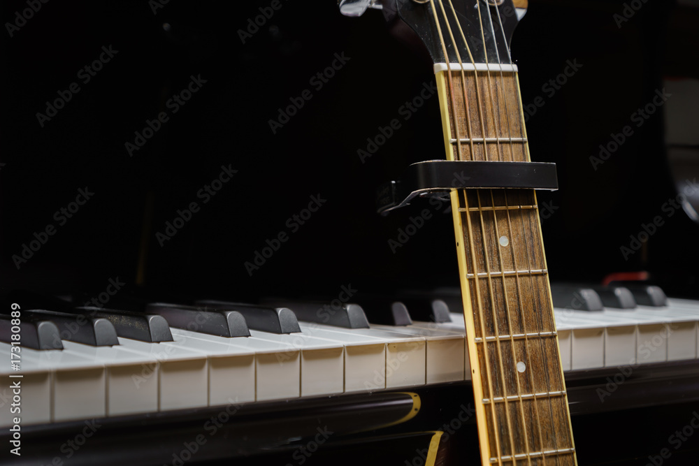 Obraz premium acoustic guitar with capo against grand piano keys - closeup musical instruments concept for musical composition and creativity