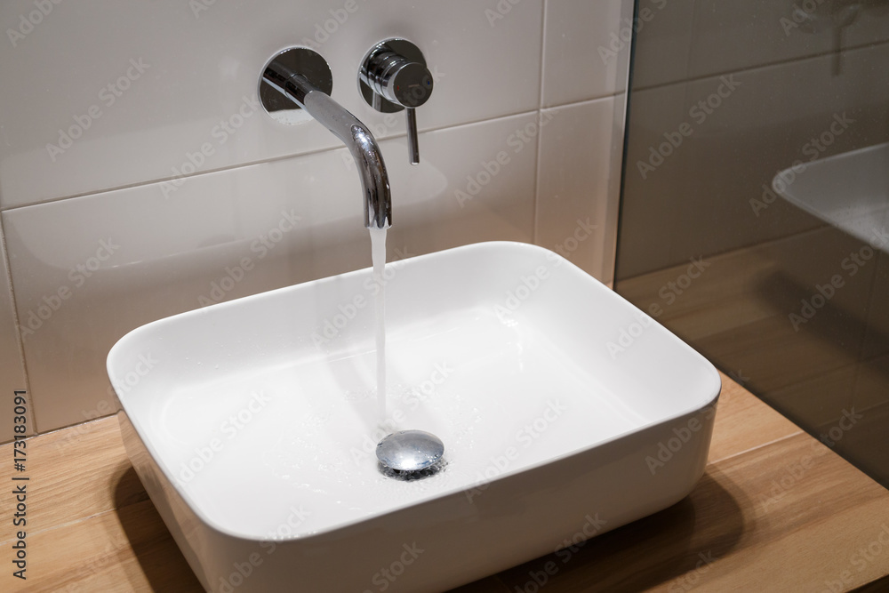 Fototapeta premium Close up of sink and faucet on wooden shelf in white bathroom interior