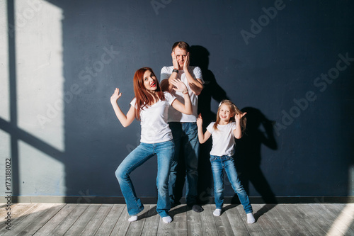 Stress dad standing with happy child and wife on gray background wooden floor room window sunny day