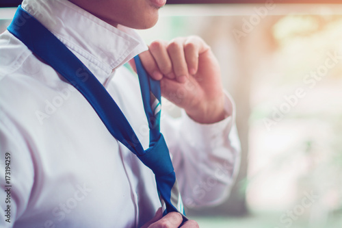 The businessman ties a black tie, in white shirt.