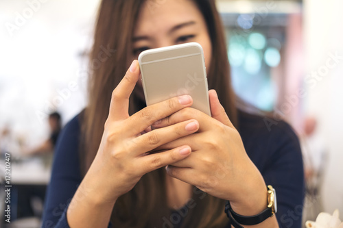 Closeup image of a beautiful Asian business woman holding , using and looking at smart phone in modern cafe