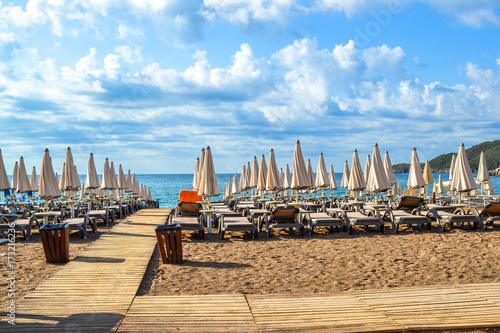 The beach of Montenegro. Sun beds and sun umbrellas in the assembled state on the beach. Clouds over the sea. The Budva Riviera. Vecici © Aleksandr