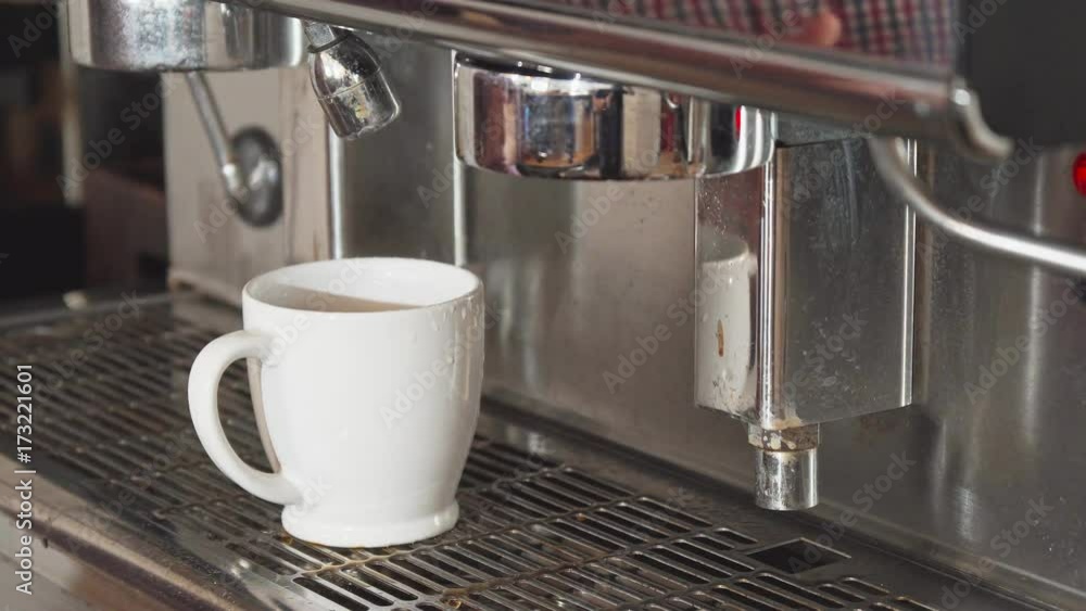 The coffee is preparing. The cup stands in the coffee machine. The coffee machine is adding some boiling water into the cup. The barista is waiting until the coffee is ready The coffee is preparing. The cup stands in the coffee machine. The coffee machine is adding some boiling water into the cup. The barista is waiting until the coffee is ready