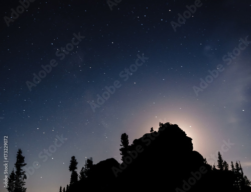 Stars in the night sky against the backdrop of silhouettes of trees and huge rocks