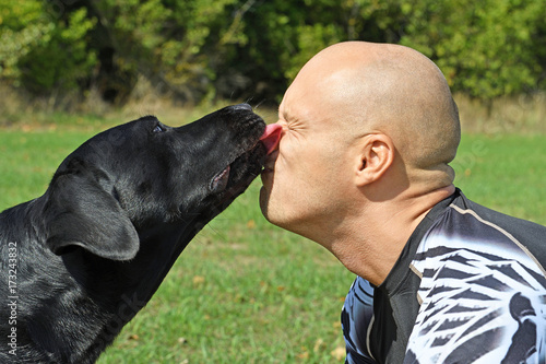 Black dog give kiss man in the park at sunny day.