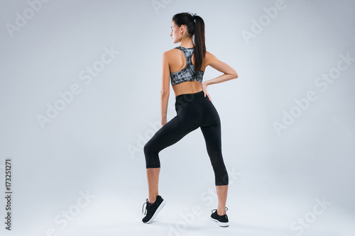 Beautiful and sexy sport woman posing as sportwoman back to the camera in studio over gray background