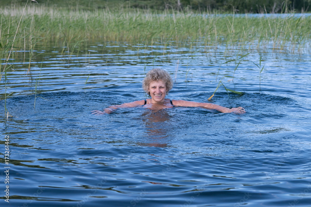 Радостная женщина среднего возраста плавает в озере.