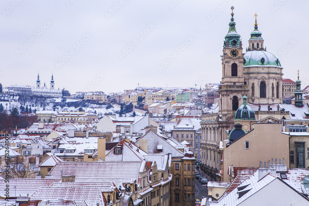 The historical center of Prague in winter. The Church of St. Nicholas in the Lesser Country is the most beautiful view from the Malostranska tower. Panorama of the city, roofs covered with snow.