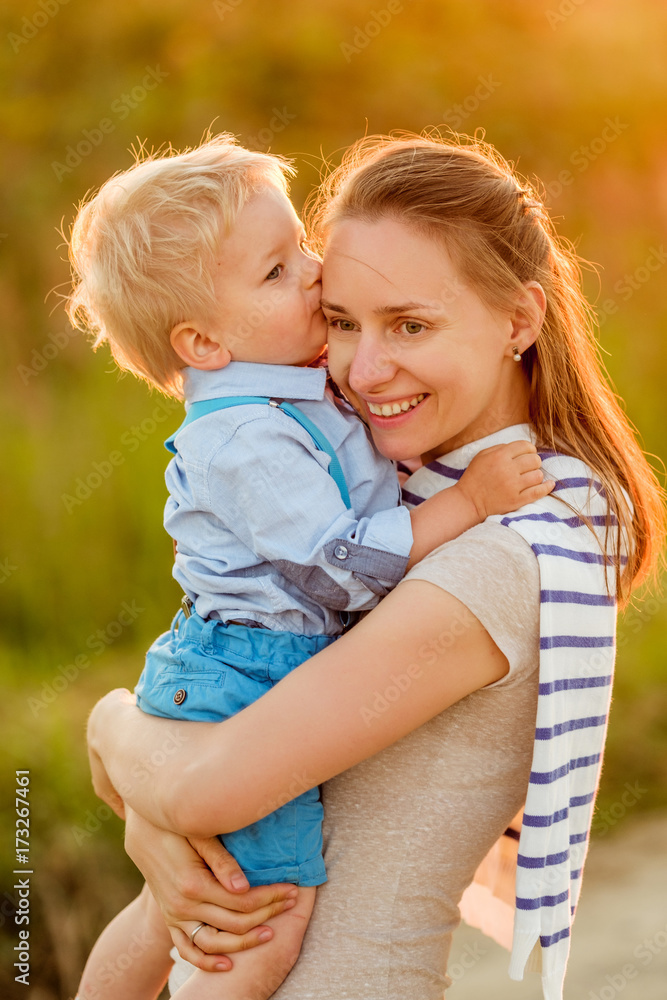 Woman and child outdoors at sunset. Boy kissing his mom. Woman and child outdoors at sunset. Boy kissing his mom.